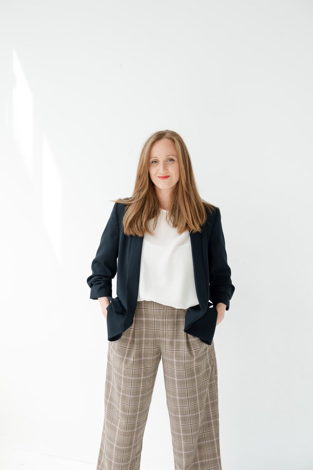 Redona Dida standing in a studio, wearing a dark blazer, white top and wide-leg plaid trousers
